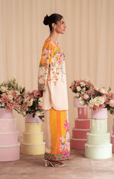 Woman in a floral outfit standing among decorated cakes and flowers.